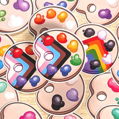 Pile of LGBTQIA+ inspired palettes. Paint on the palettes represents each flag, including Ally, Progress, and simple Rainbow.