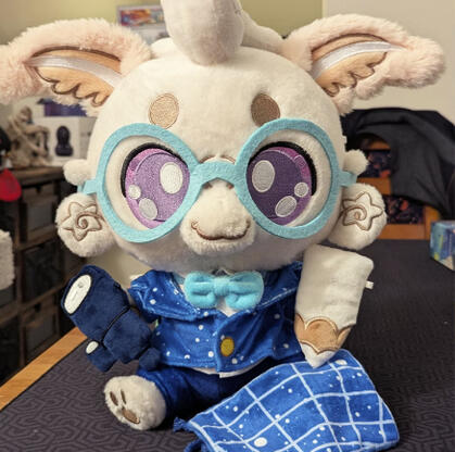 Laisy Luna Moth Plushpanion: A white mothy plush sits on a black mat. The white fluffy moth is wearing light blue glasses, a star (white dot) cobalt blue blazer, with matching navy blue trousers. They're holding a white pencil and dark blue telescope prop.